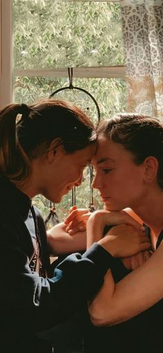 two women are touching each other in front of a window