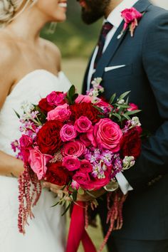 a bride and groom holding a bouquet of red roses