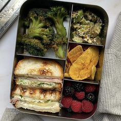 an open lunch box with broccoli, raspberries, and other foods