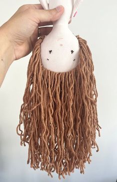 a hand holding a stuffed animal with long dreadlocks on it's head