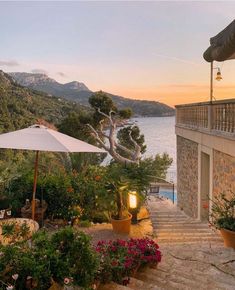 an outdoor patio with tables and umbrellas next to the water at sunset or dawn