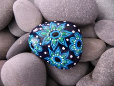 a blue and green painted rock sitting on top of some gray rocks with white dots