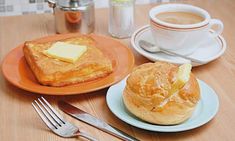 two plates with bread and butter on them next to a cup of coffee