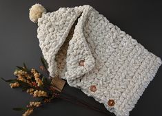 a white crocheted blanket with buttons and a flower on the table next to it