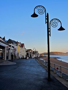 an empty street next to the ocean with people walking on it and buildings in the background