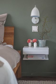 a nightstand with flowers on it next to a bed in a green walled bedroom area