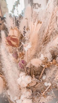 an arrangement of dried flowers and feathers in a vase