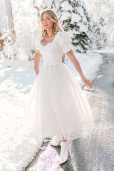 a woman in a white dress standing on the side of a road covered in snow