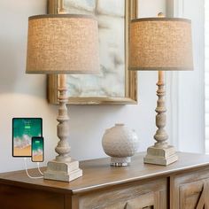 two lamps sitting on top of a wooden dresser next to a cell phone and tablet