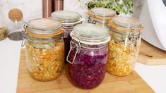 four jars filled with food sitting on top of a wooden cutting board