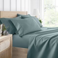 a bed with blue sheets and pillows next to a night stand on a wooden table