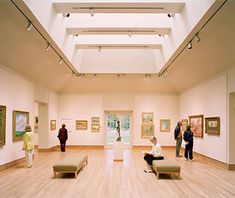 people are looking at paintings on display in an art gallery with wooden floors and skylights