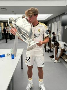 a young man holding a soccer trophy while standing in front of a table with other people