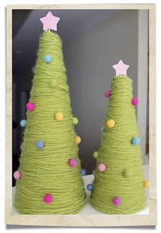 two green christmas trees made out of yarn with pink stars on top and blue balls around them