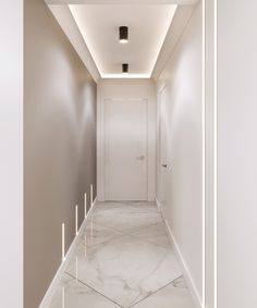 an empty hallway with white walls and marble flooring is lit by recessed lighting