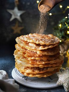 a stack of pancakes being sprinkled with sugar on a plate next to a christmas tree