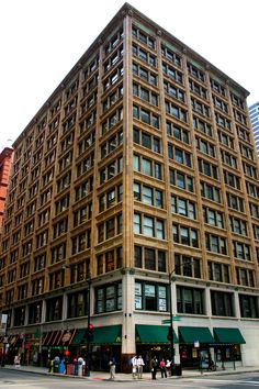 a tall building sitting on the corner of a street with people walking around it and buildings in the background