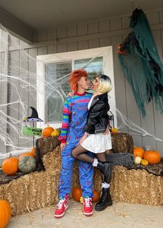 two people dressed in costumes standing next to hay bales with pumpkins on them