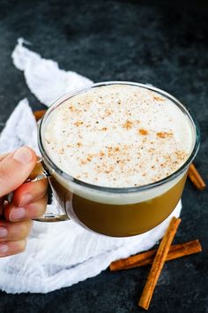 a hand holding a cup of coffee with cinnamon sticks around it