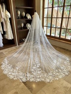 a wedding veil hanging in front of a window with white flowers on the floor next to it