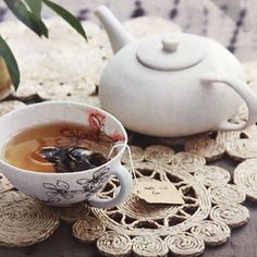 a cup of tea on a doily next to a teapot