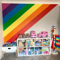 a room with a rainbow painted wall next to a book shelf filled with books and toys