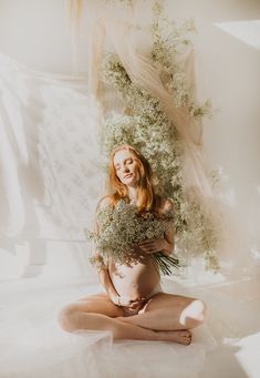 a pregnant woman sitting on the floor holding flowers