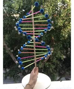 a hand is holding a stick with many colored balls on it in the shape of a tree