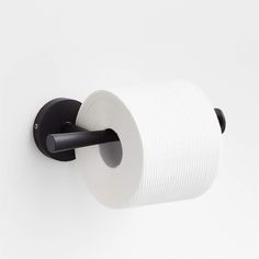 a roll of toilet paper is hanging on the wall next to a black holder with two rolls of toilet paper in it