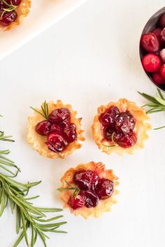 small cranberry tarts with rosemary sprigs next to them on a white surface