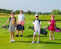 four young people standing on top of a green field holding golf clubs and ball bags