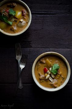 three bowls filled with soup on top of a wooden table next to a fork and knife