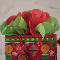 a red gift bag with green tissue flowers in it