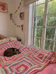 a cat laying on top of a crocheted bed in a bedroom next to a window