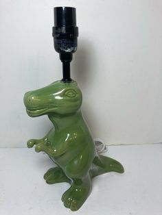 a green ceramic frog sitting on its hind legs with a plug in it's mouth