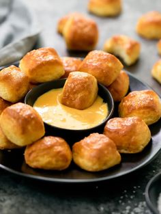 a black plate topped with rolls covered in cheese and dipping sauce next to other rolls