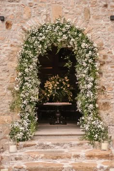 an archway with flowers and greenery in front of a stone building entrance to a wedding ceremony