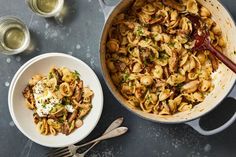 a pan filled with pasta and sauce next to two glasses