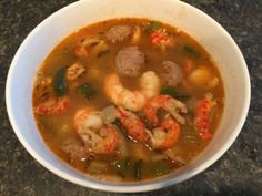 a bowl of soup with shrimp, sausage and other foods in it on a table