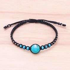 a blue beaded bracelet with black cord and turquoise beads on a wooden table top