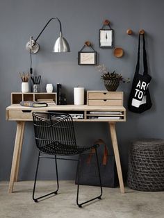 a wooden desk topped with a black chair next to a wall filled with framed pictures