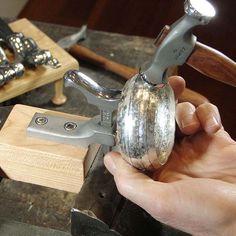 a person holding a metal object in their hand near other tools on a workbench