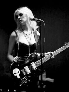 a woman holding a guitar while standing in front of a microphone