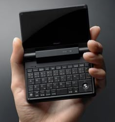 a person holding up a laptop computer in their left hand, with the keyboard open