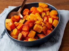 a bowl filled with cooked carrots on top of a wooden table next to a spoon