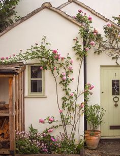 a small white house with pink flowers growing on the front and side of it's door