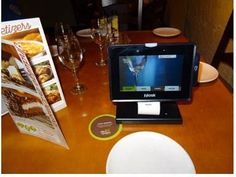 a tablet computer sitting on top of a wooden table next to wine glasses and menus