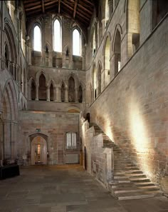 the inside of an old building with stone floors and arches on the walls, along with stairs leading up to two large windows