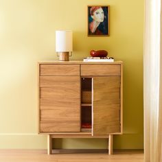 a wooden cabinet sitting next to a lamp on top of a hard wood floor in front of a yellow wall