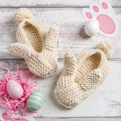 two crocheted baby shoes next to an easter egg on a white wooden table